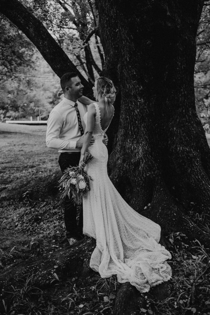 Gold Coast Wedding photographer, intimate moment with bride and groom. Standing under a large tree at their wedding at Sol Gardens. Her dress flows over the roots of the tree.