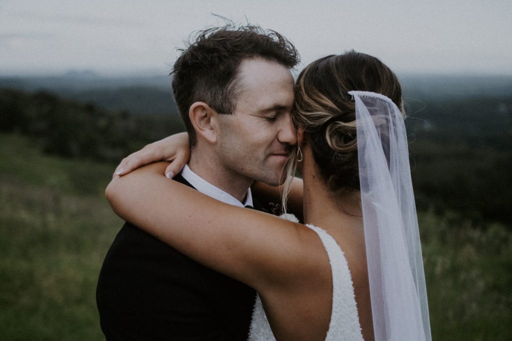 Groom snuggles into bride as she wraps her arms around him during wedding photos on the Sunshine Coast