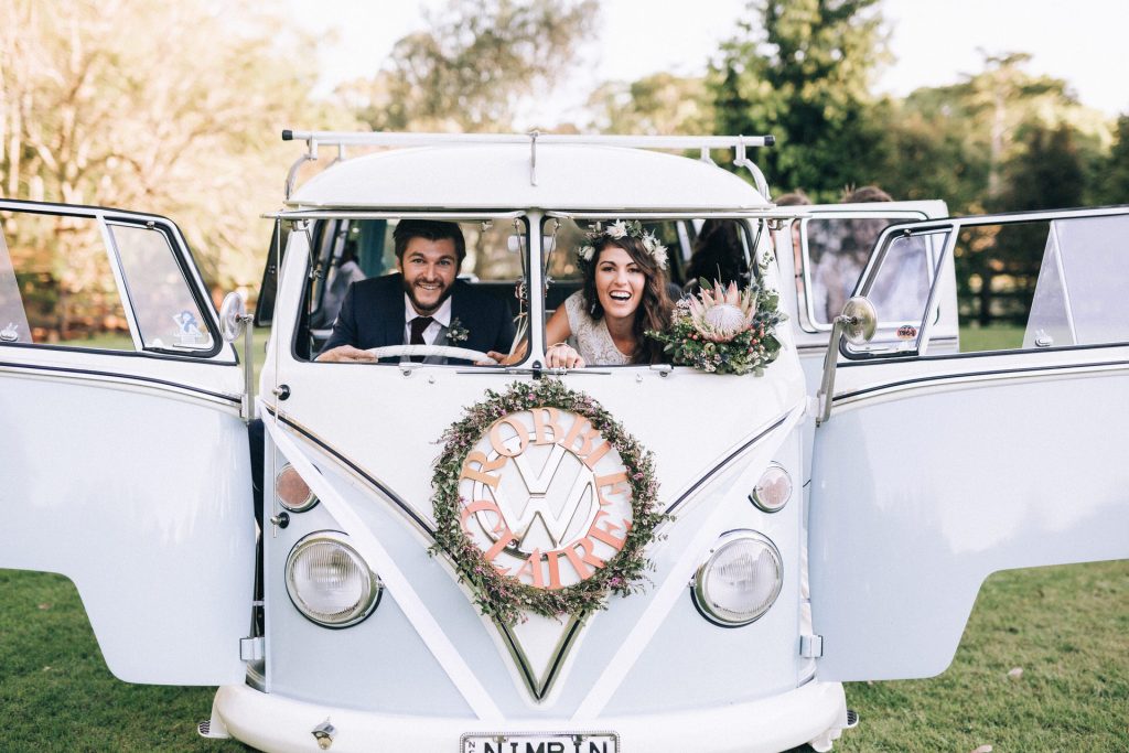 Byron Bay wedding photographer, couple on their wedding day laughing as they peer through open windows of a vintage volkswagen combi van.