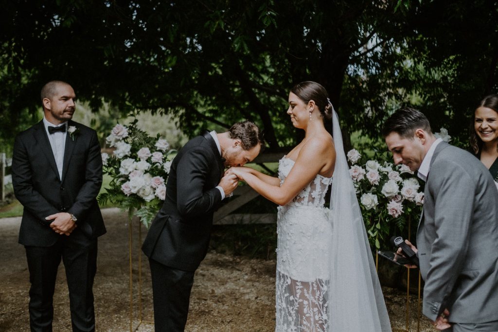 Byron Bay wedding groom takes the brides hands and kisses them bowing slightly to her.