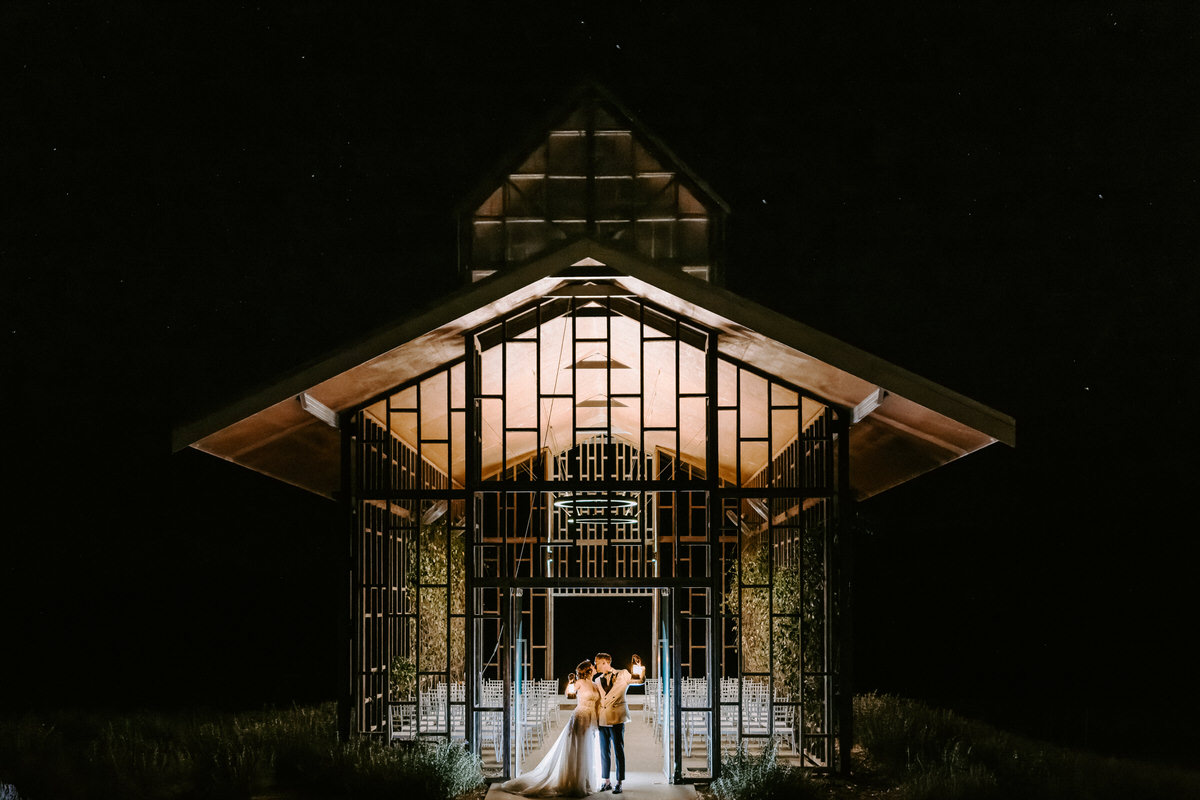 Scenic Rim Wedding Guide- Bride and groom standing infront of open air chapel at night with lanterns with a stars in the sky