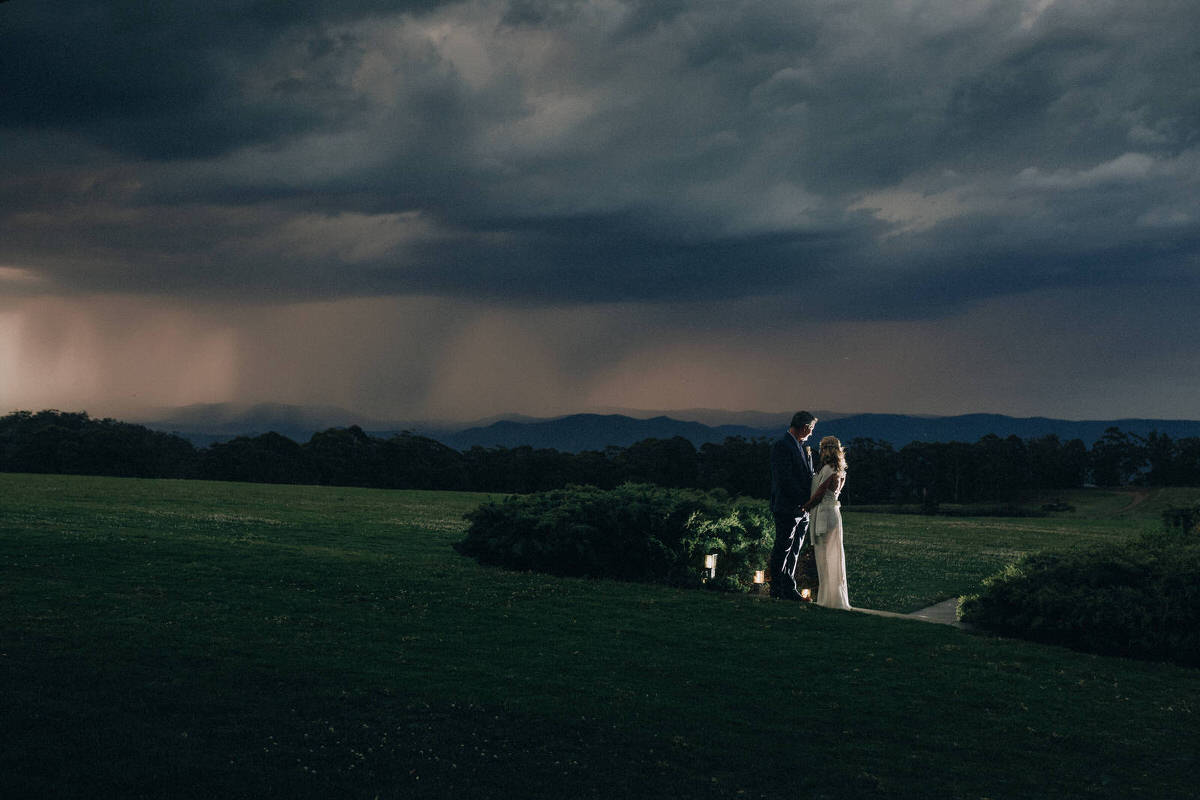 Stormy night after wedding at Spicers Peak lodge a bride and groom stand outside looking at the rain storm in the distance